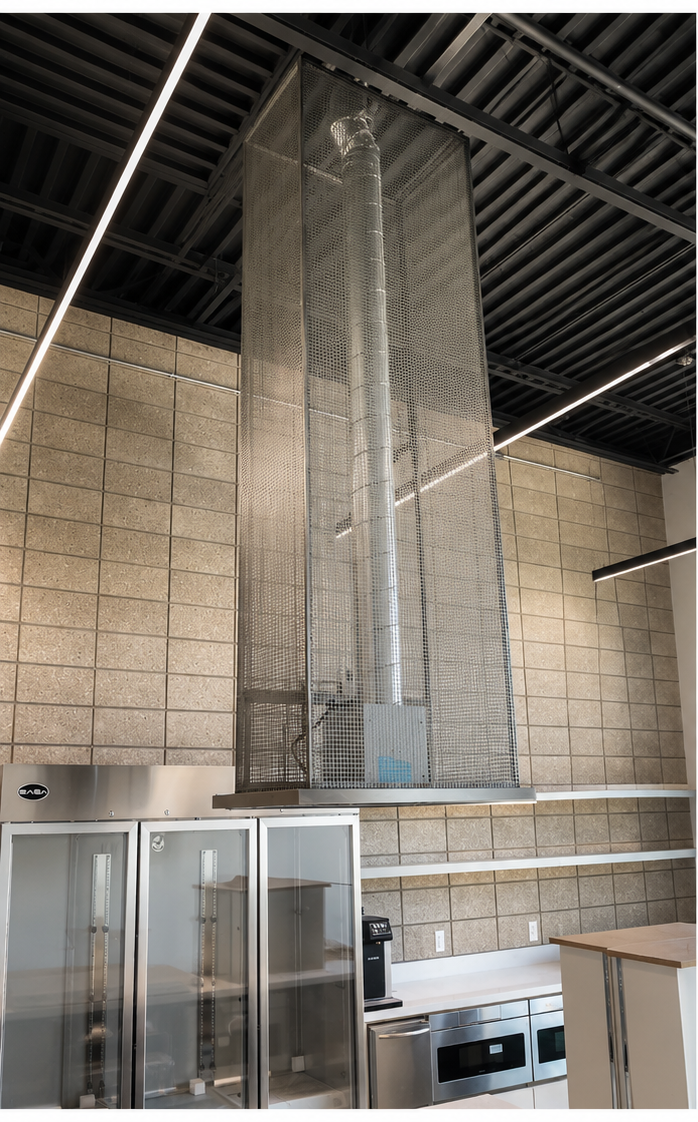 Tall perforated stainless mesh pendant shroud suspended in a café interior