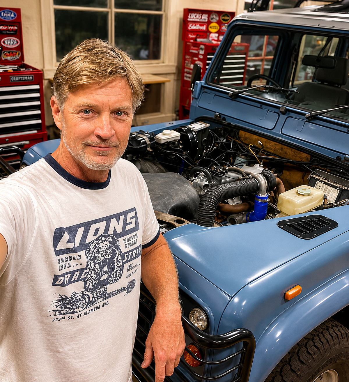 Michael Tilly beside a blue Land Rover Defender with its hood open in the shop
